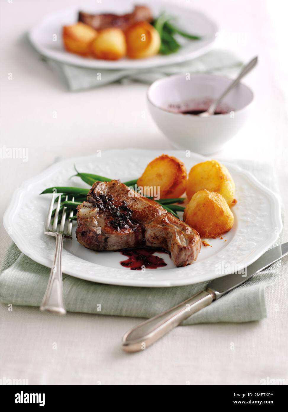 Gegrillte Lammkoteletts mit französischen Bohnen, Bratkartoffeln und roter Johannisbeersoße Stockfoto