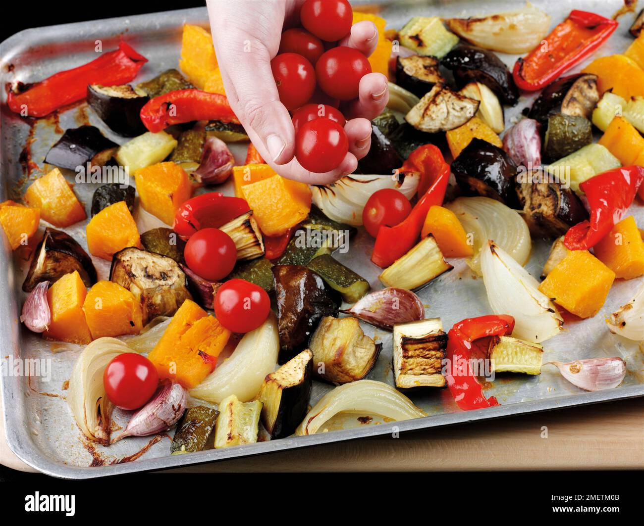 Zugabe von Kirschtomaten zu geröstetem Gemüse (Zucchini, Auberginen, Zwiebeln, rote Paprika, Butternusskürbis, Knoblauch) und weitere fünf Minuten rösten Stockfoto
