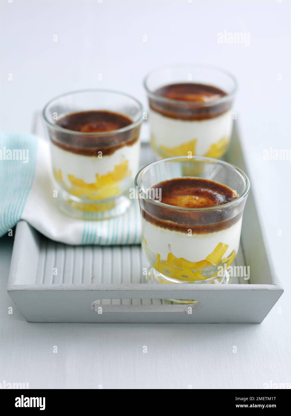 Gekühlte Mango-, Joghurt- und Frischkäse-Desserts, mit Moschuszucker bestreut, serviert in Gläsern auf einem Serviertablett Stockfoto