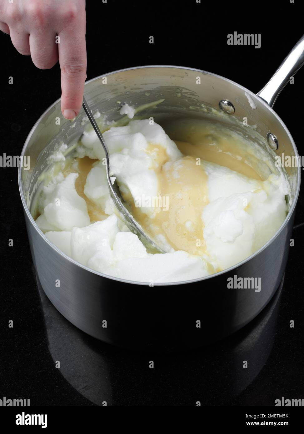 Käsesoufflés zubereiten, Eiweiß zur Mischung hinzufügen und mit einem Löffel zusammenfalten Stockfoto