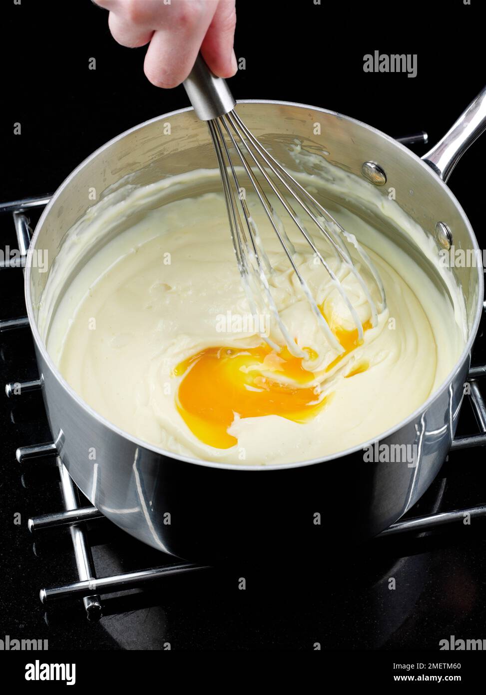 Käse-Soufflés machen, Eigelb zu heißer Sauce rühren, ein Eigelb nach dem anderen Stockfoto