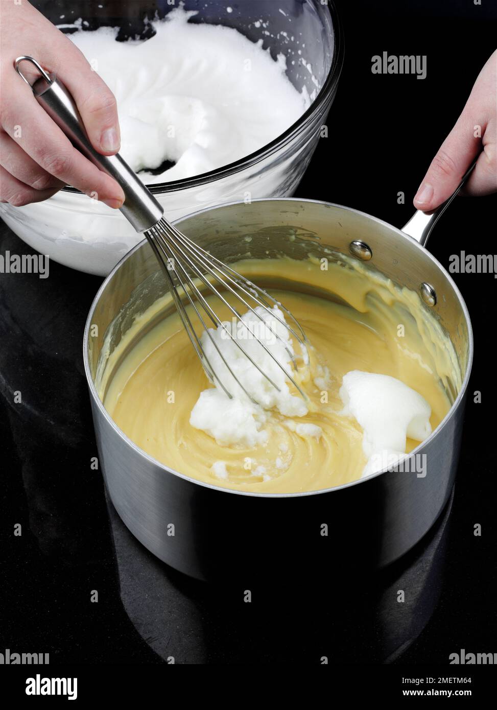Käse-Soufflés zubereiten, Eiweiß zur gekühlten Sauce hinzufügen und Mischung mit Schneebesen schlagen Stockfoto