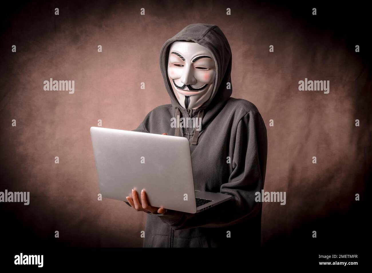 Mann mit anonymer Maske, Sweatshirt und Laptop, Studiofoto Stockfoto