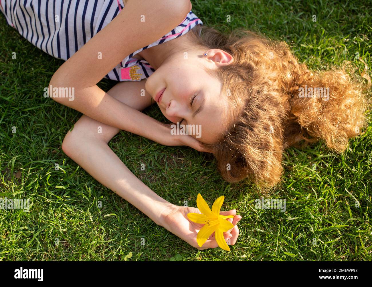 Ein süßes Mädchen mit 11-12 Jahren schläft an einem sonnigen Tag auf grünem Gras. Erholen Sie sich im Sommer in der Natur. Tag der Erde. Unachtsamkeit, Harmonie, Idylle, Gelassenheit. Sunba Stockfoto
