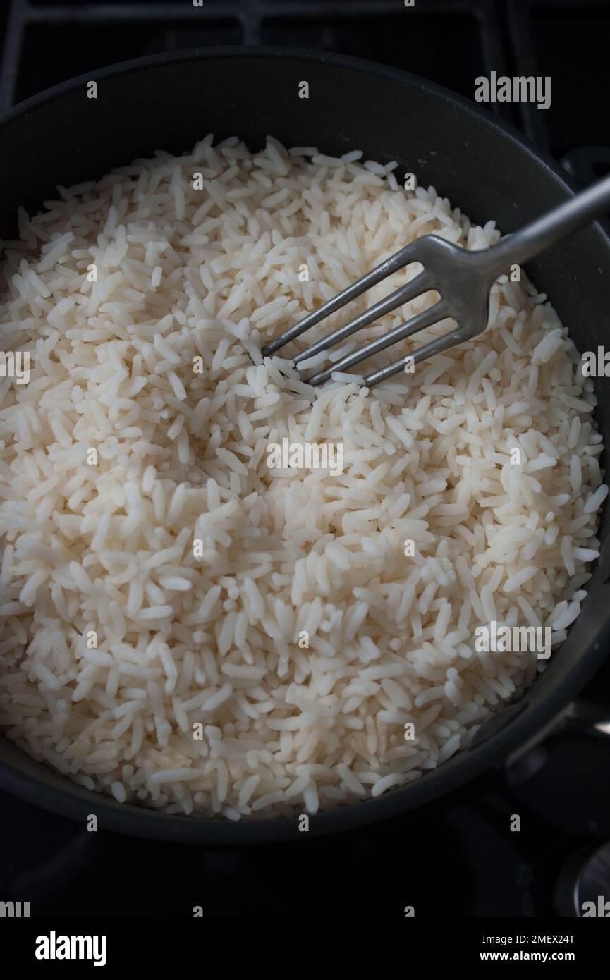 Wie man flauschigen Reis jedes Mal kocht, Schritt 3: Gekochter Reis in einer Pfanne, eine Gabel wird verwendet, um den Reis aufzufusseln Stockfoto