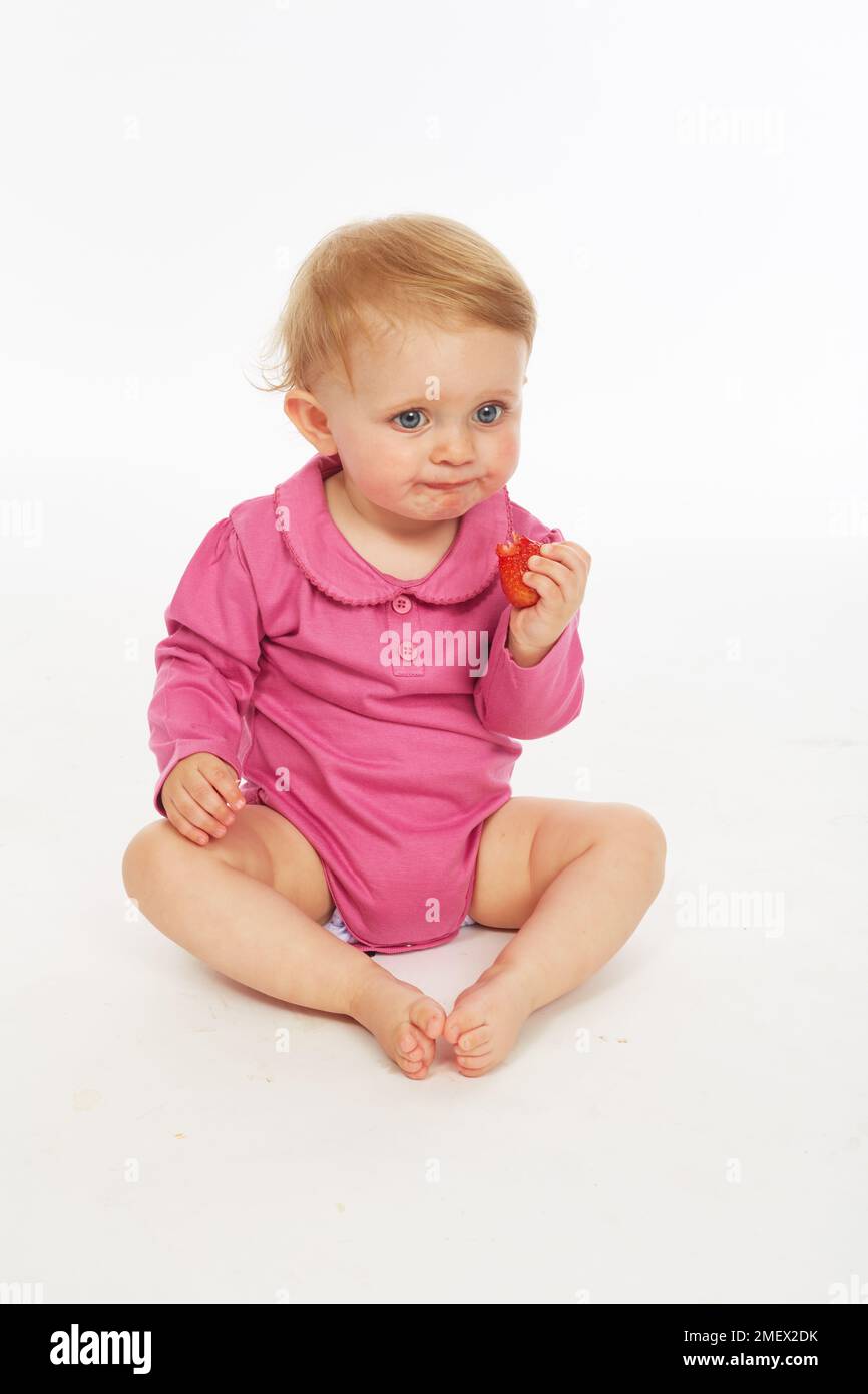 Baby in rosa Strampler essen Erdbeere (Modell Alter - 9 Monate) Stockfoto