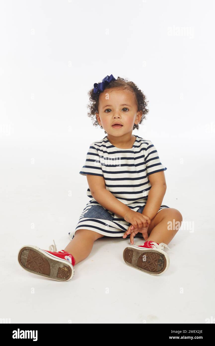 Kleines Mädchen in gestreiftem Kleid spielt, verschiedene Posen (Modellalter – 19 Monate) Stockfoto