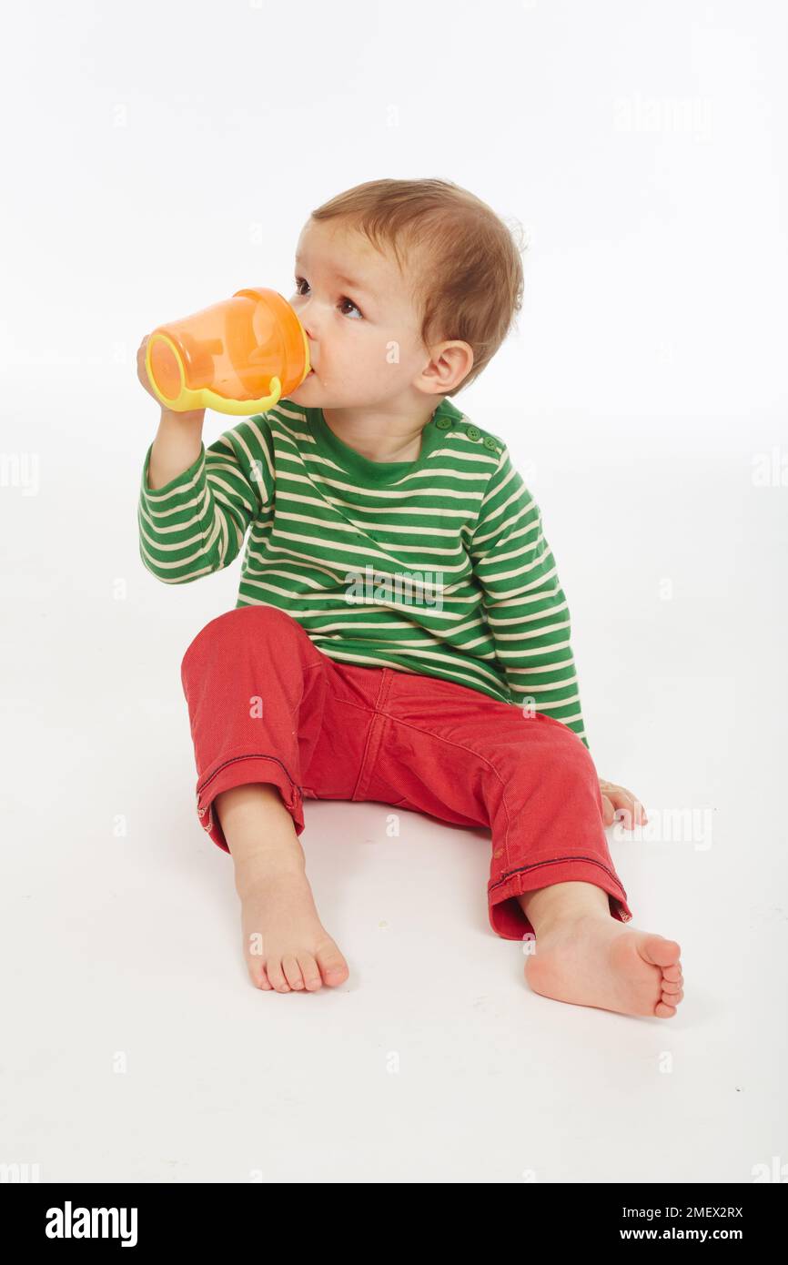 Kleiner Junge in grün gestreiftem Oberteil mit Becher (Modellalter – 22 Monate) Stockfoto