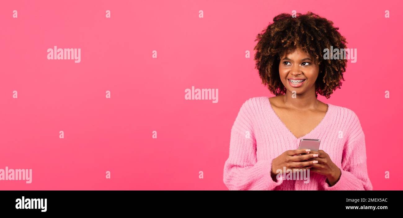 Eine fröhliche, afroamerikanische Dame mit Zahnspange, die ganz zwanglos auf dem Telefon tippt, schaut auf die Kopierfläche Stockfoto