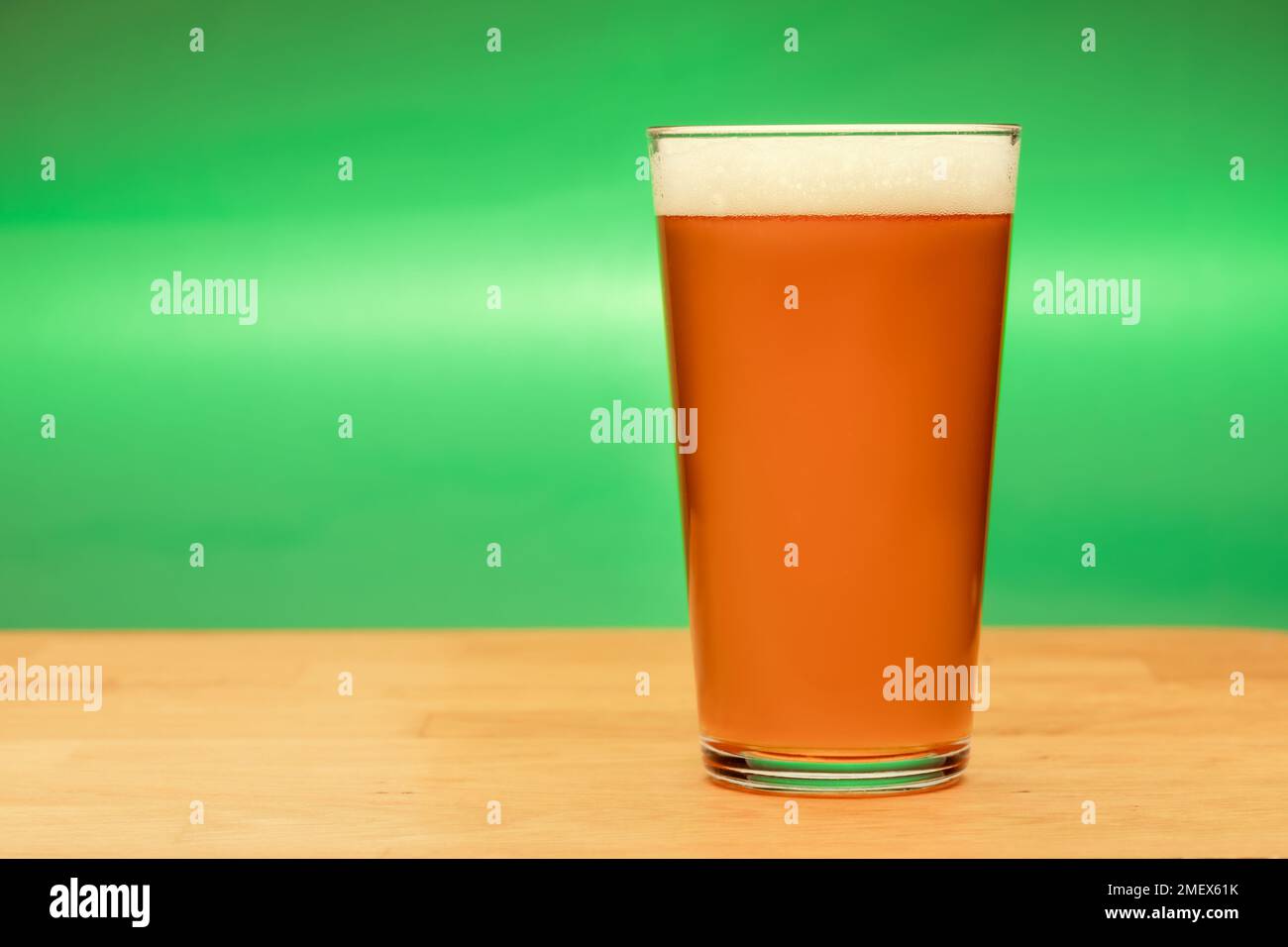 Volles Shaker Pint Glas Amber Ale oder Bier auf Holztisch mit grünem Hintergrund Stockfoto