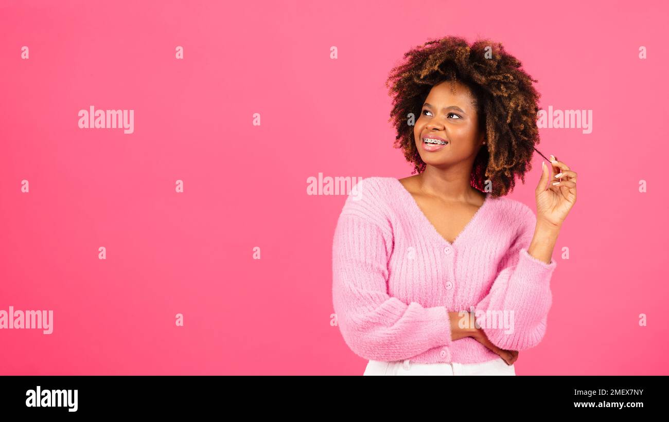 Fröhliche, überraschende, afroamerikanische, lockige Millennials-Frau mit einer Zahnspange in lässiger Optik, die sich einen Kopierbereich ansieht Stockfoto