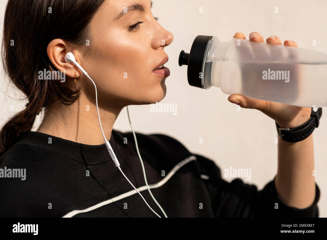 Eine ernsthafte junge sportlerin in sportbekleidung und Kopfhörern, die Wasser aus der Flasche trinkt, entspannt Stockfoto