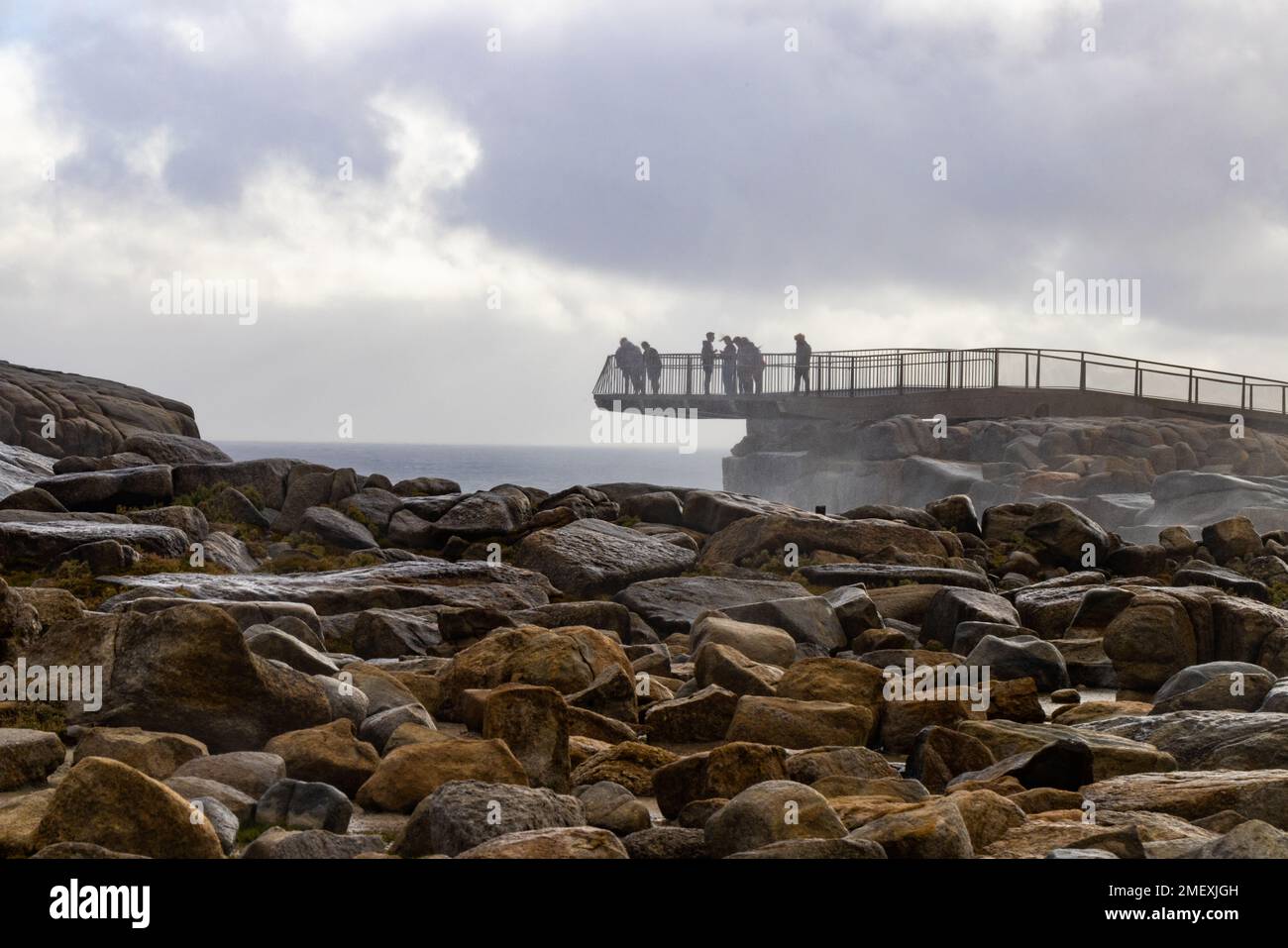 Eine Gruppe von Menschen traut sich kaltem, windigen Wetter, um die Lücke von einer freitragenden Aussichtsplattform zu betrachten, die von Felsen in der Nähe von Albany in Westaustralien unterstützt wird Stockfoto