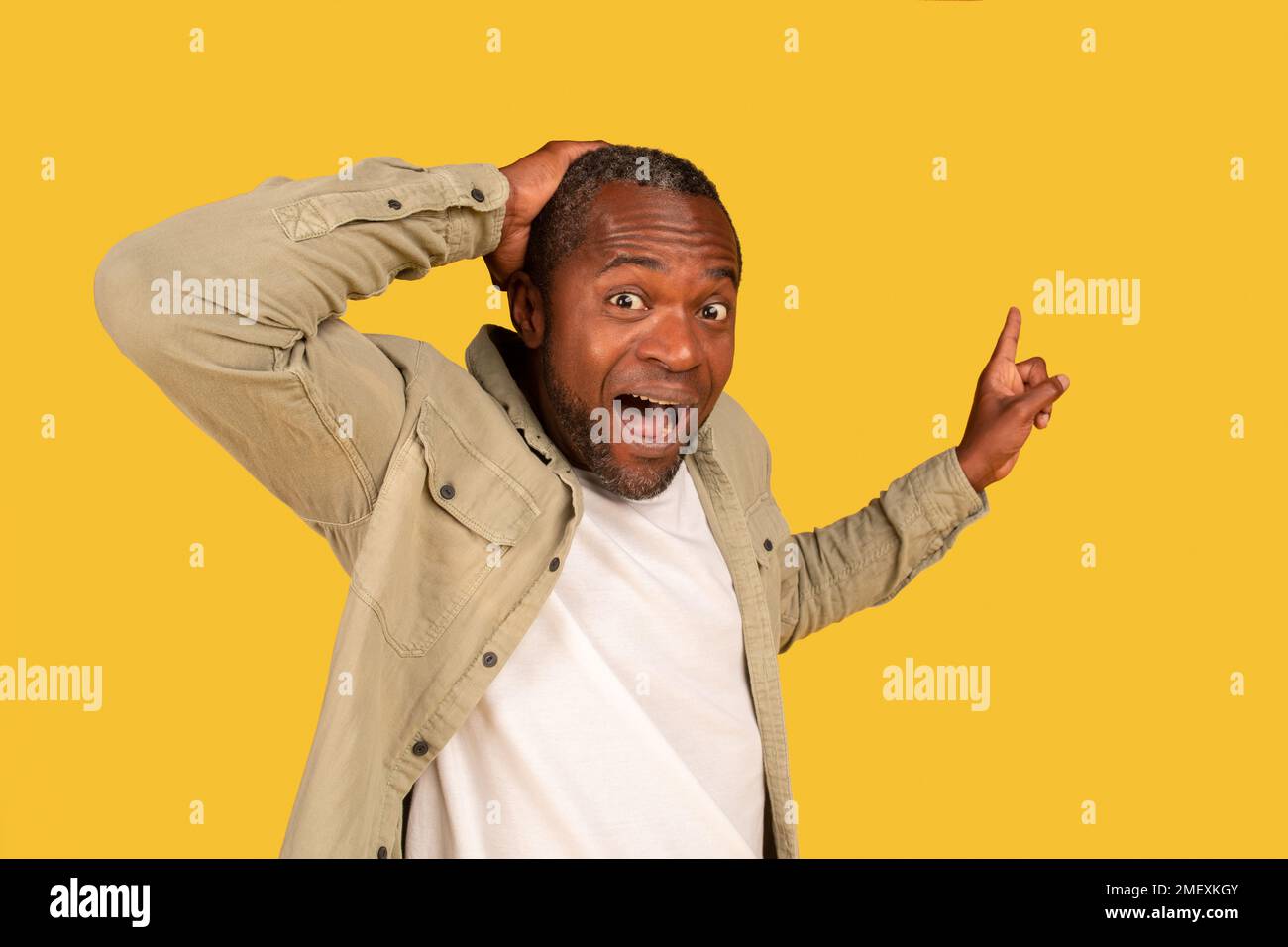 Porträt eines zufriedenen, überraschten, reifen schwarzen Mannes mit offenem Mund, Hand an Kopf halten, Finger an freien Platz zeigen Stockfoto