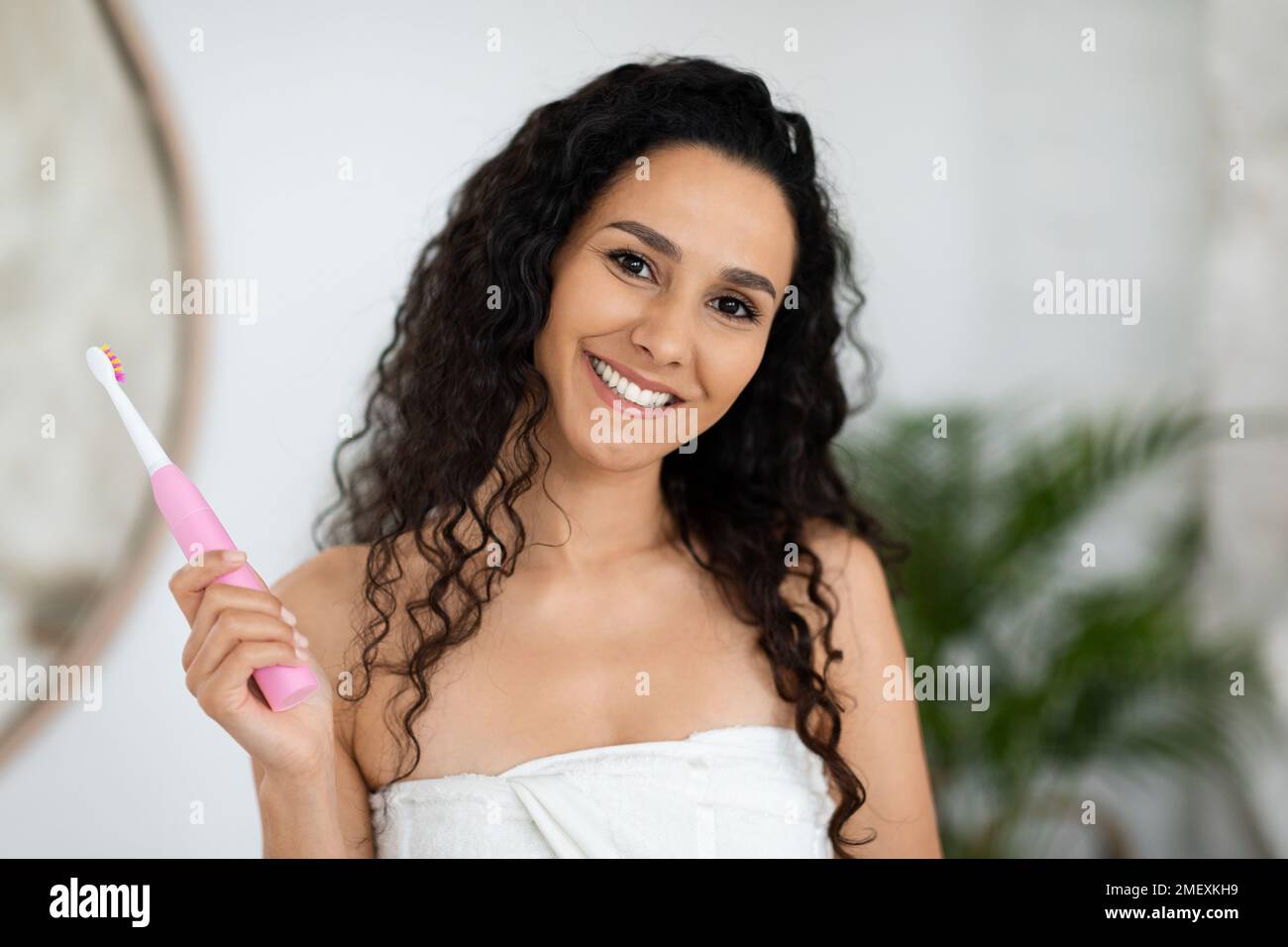 Lächelnde arabische Millenial Lady im Handtuch mit schneeweißen Zähnen perfekte Zahnbürste halten, Mundhygiene genießen Stockfoto