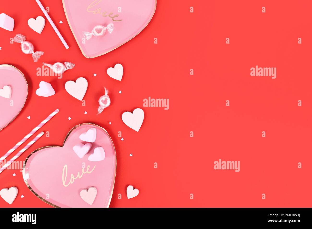 Valentinstag-Flachbett mit herzförmigen Tellern, Herzverzierungen und Süßigkeiten auf pinkfarbenem Hintergrund Stockfoto