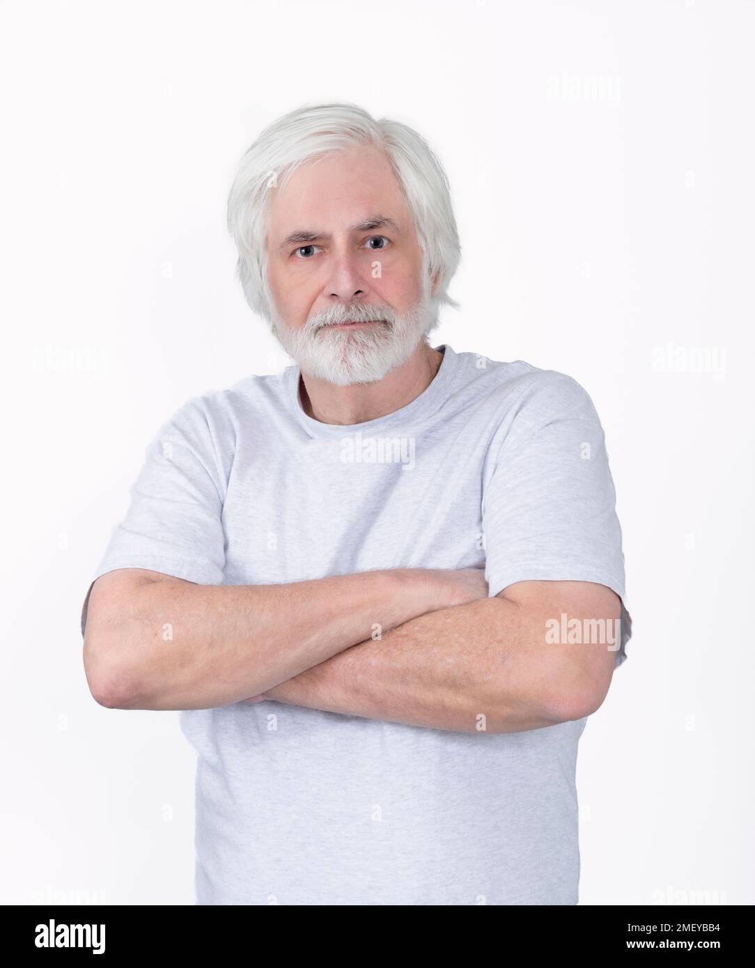Vertikaler Schuss eines schmuddeligen, aber selbstbewussten alten Mannes mit verschränkten Armen. Von der Hüfte nach oben. Weißer Hintergrund. Stockfoto
