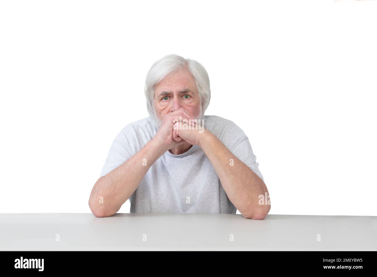 Horizontale Aufnahme eines besorgten, weißhaarigen alten Mannes, der mit seinen Ellbogen auf dem Tisch sitzt. Weißer Hintergrund. Viel Platz zum Kopieren. Stockfoto