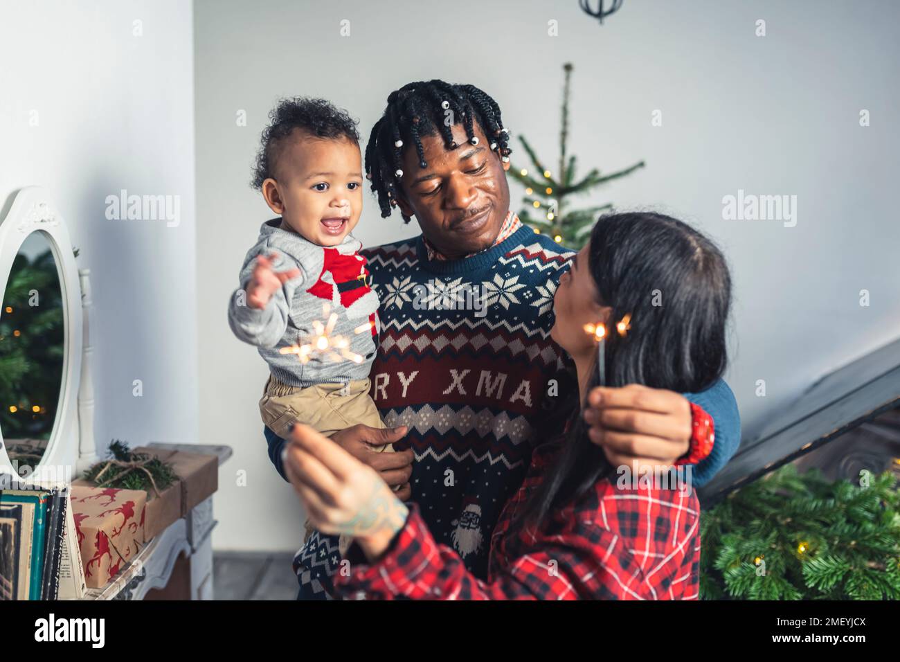 Multikulturelle Eltern und ihr Kleinkind mit Weihnachtsfeuerstäbchen. Hochwertiges Foto Stockfoto
