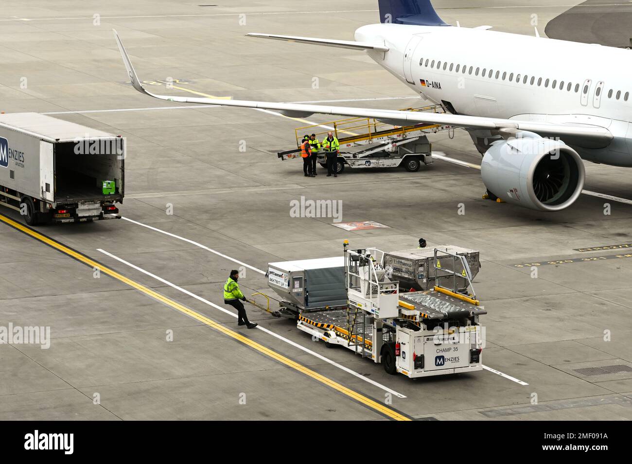 London, England - April 2022: Flughafenarbeiter, der eine Frachtpalette neben einem Palettenladerfahrzeug zieht Stockfoto