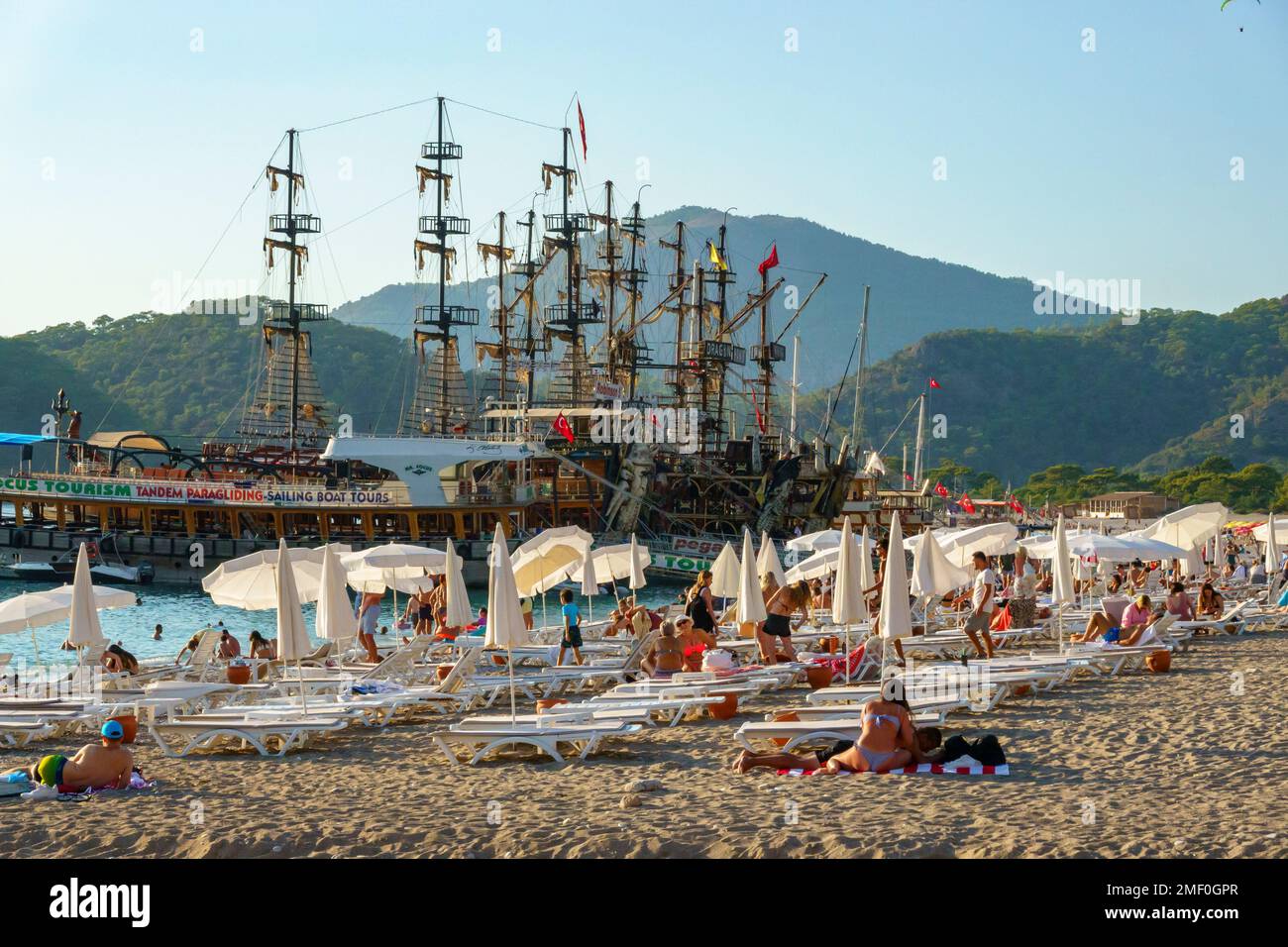Strandbesucher und piratenschiffförmige Tourboote in Belcekiz Beach, Oludeniz, Fethiye, Türkei Stockfoto
