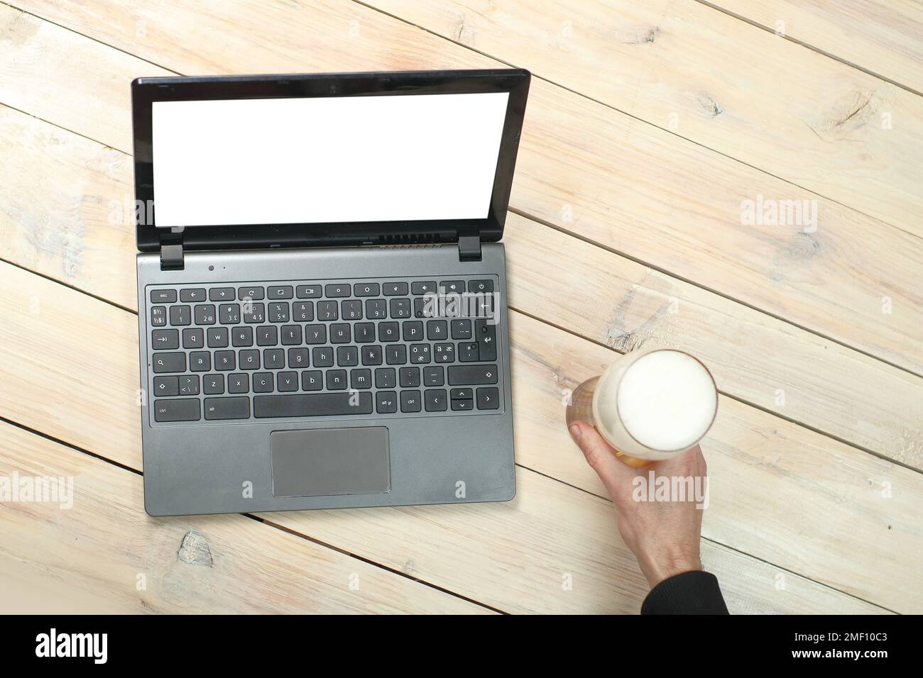 Grauer Laptop auf einem Holztisch neben einem Bierbecher und einer Hand Stockfoto