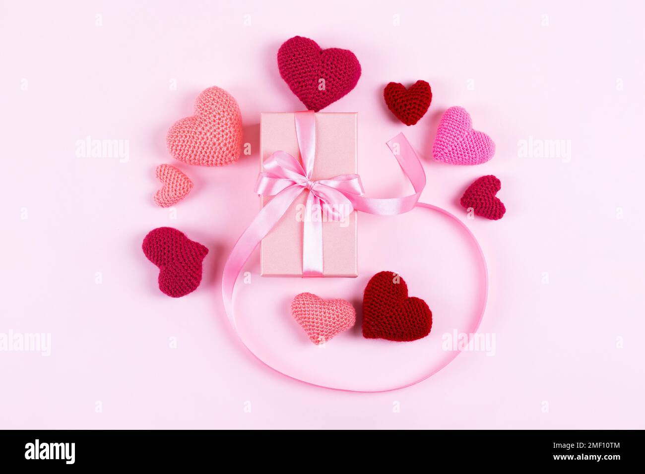 Grußkarte zum Valentinstag, Muttertag und Geburtstag. Gestrickte pinkfarbene Herzen und Geschenkbox mit Schleife aus Satin auf pinkfarbenem Hintergrund Stockfoto