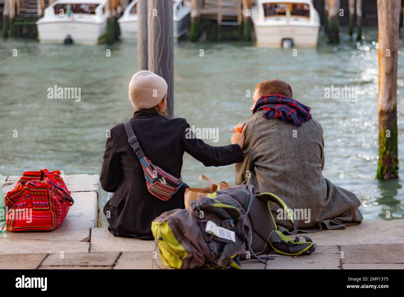 Junge Mann und Frau, die sich unterhalten, sitzen am Kanal im Herbst, Venedig, Italien. Stockfoto