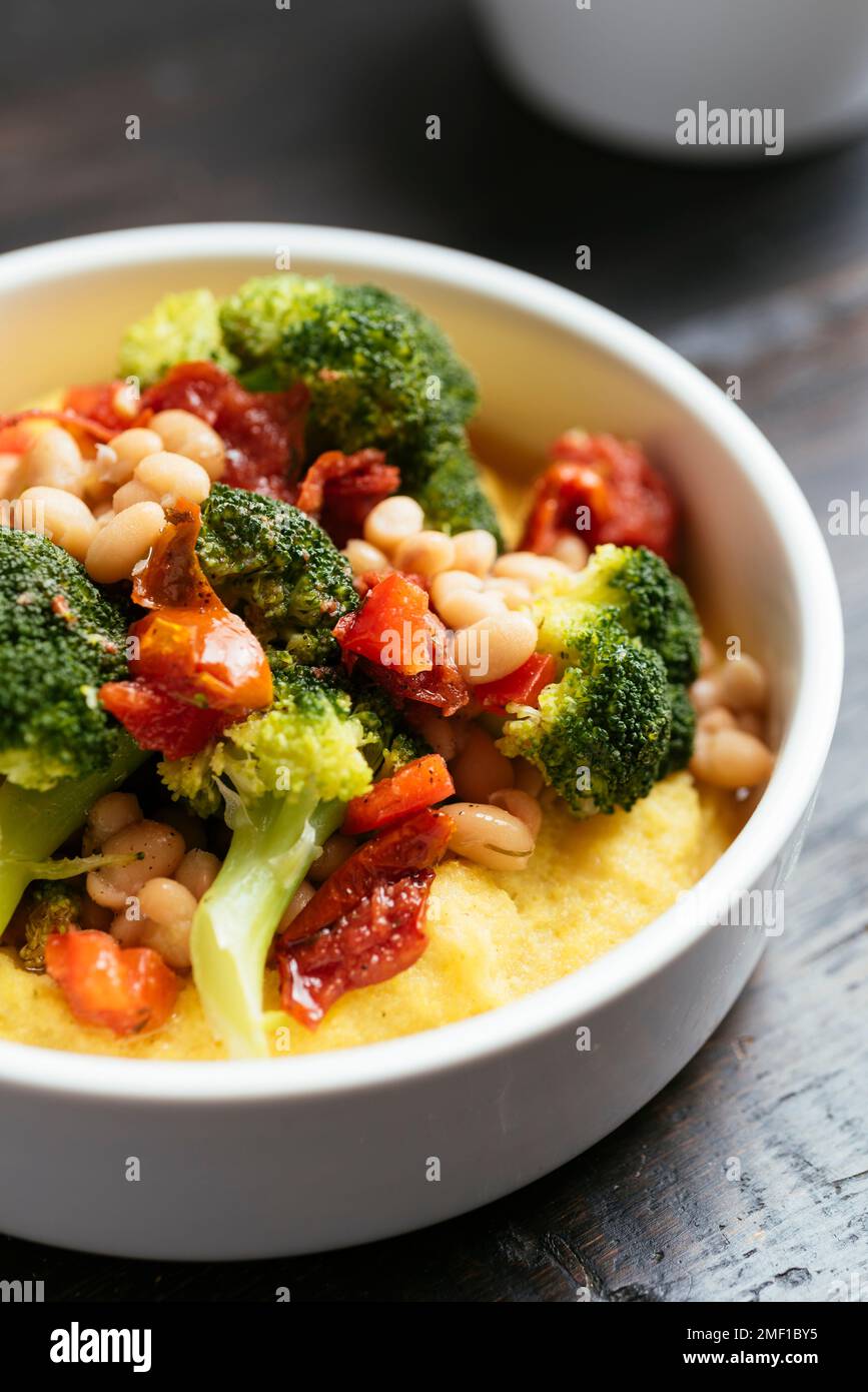 Brokkoli und Bohnen auf Polenta mit getrockneten Tomaten und Paprika. Stockfoto