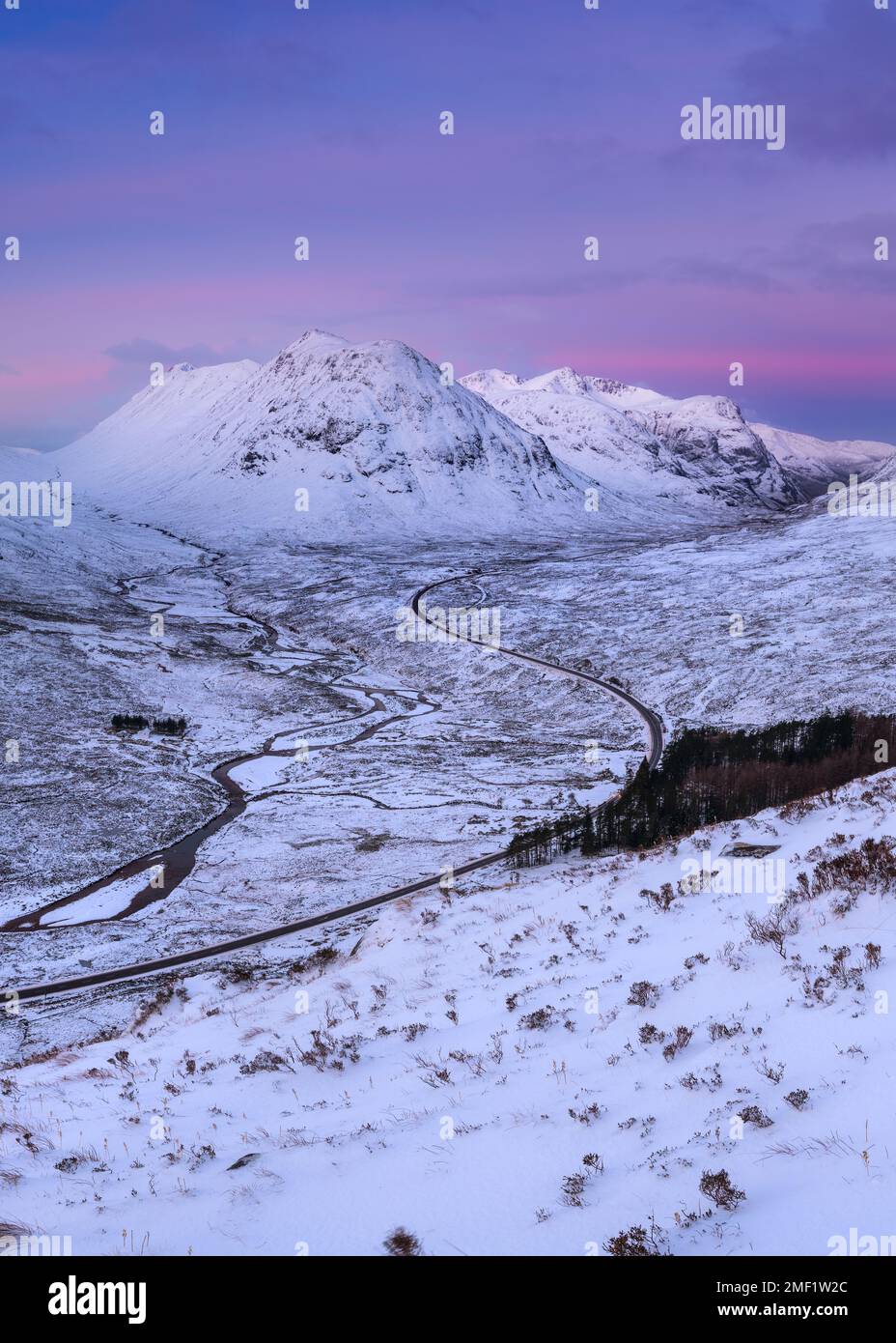 Schneebedeckte Berge von Glencoe bei Sonnenaufgang mit kurviger Straße, die durch die Landschaft führt. Scottish Highlands, Großbritannien. Stockfoto
