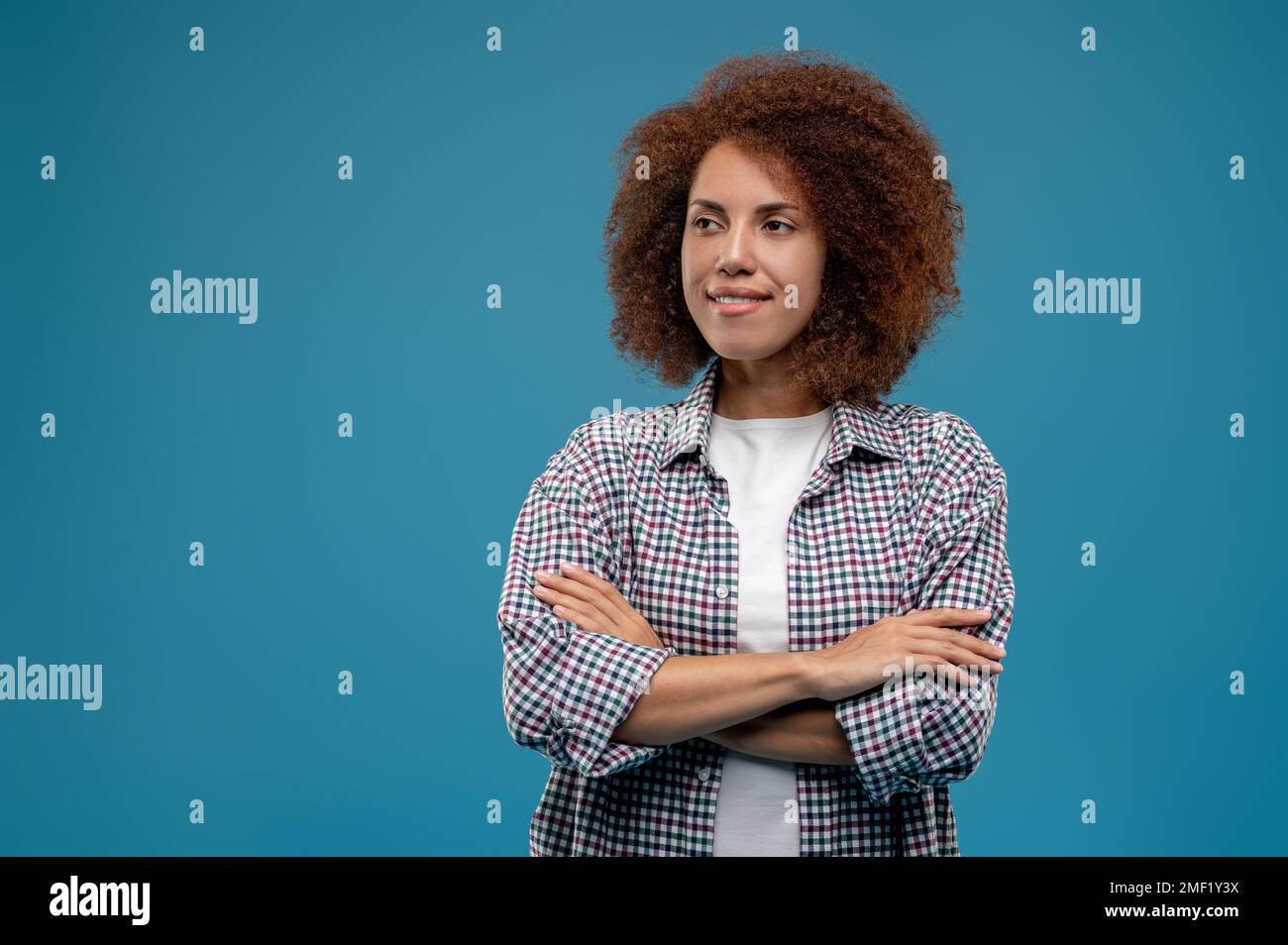 Selbstbewusste, lockige Frau, die mit gekreuzten Händen steht Stockfoto