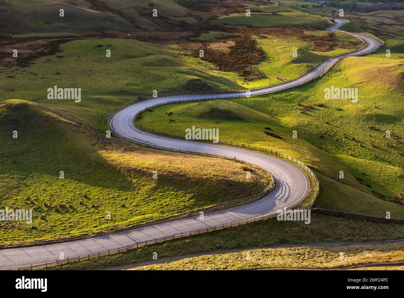 Lange gewundene Straße, die an einem Sommernachmittag im Peak District, Großbritannien, durch üppig grüne britische Landschaft führt. Stockfoto
