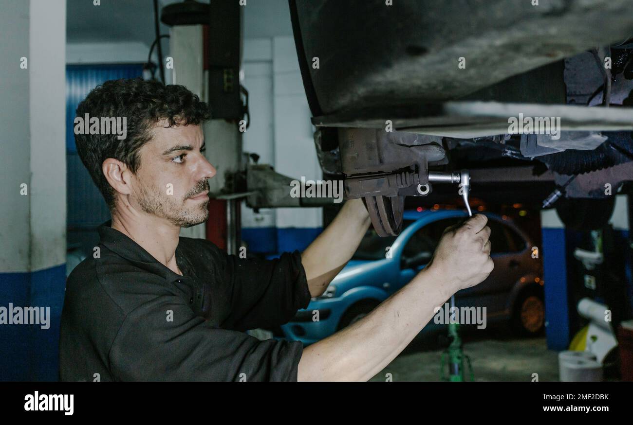 Seitenansicht erfahrener männlicher Mechaniker mit Ratsche zur Einstellung der Details der Bremsscheibe des Fahrzeugs bei der Arbeit in der Garage Stockfoto