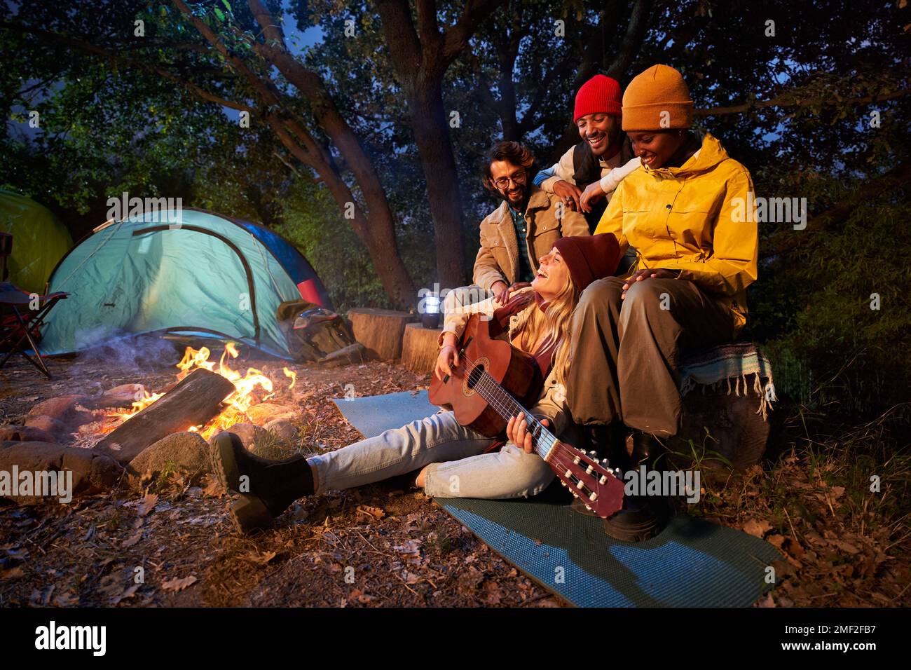 Gruppe von Freunden mit Gitarre am Lagerfeuer und Campingzelt im Freien am Nachmittag. Stockfoto