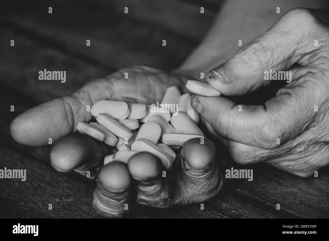Großmutter hält gelbe Pillen in den Händen auf einem Holztisch, Pillen in den Händen und Frauen liegen und Medizin Stockfoto
