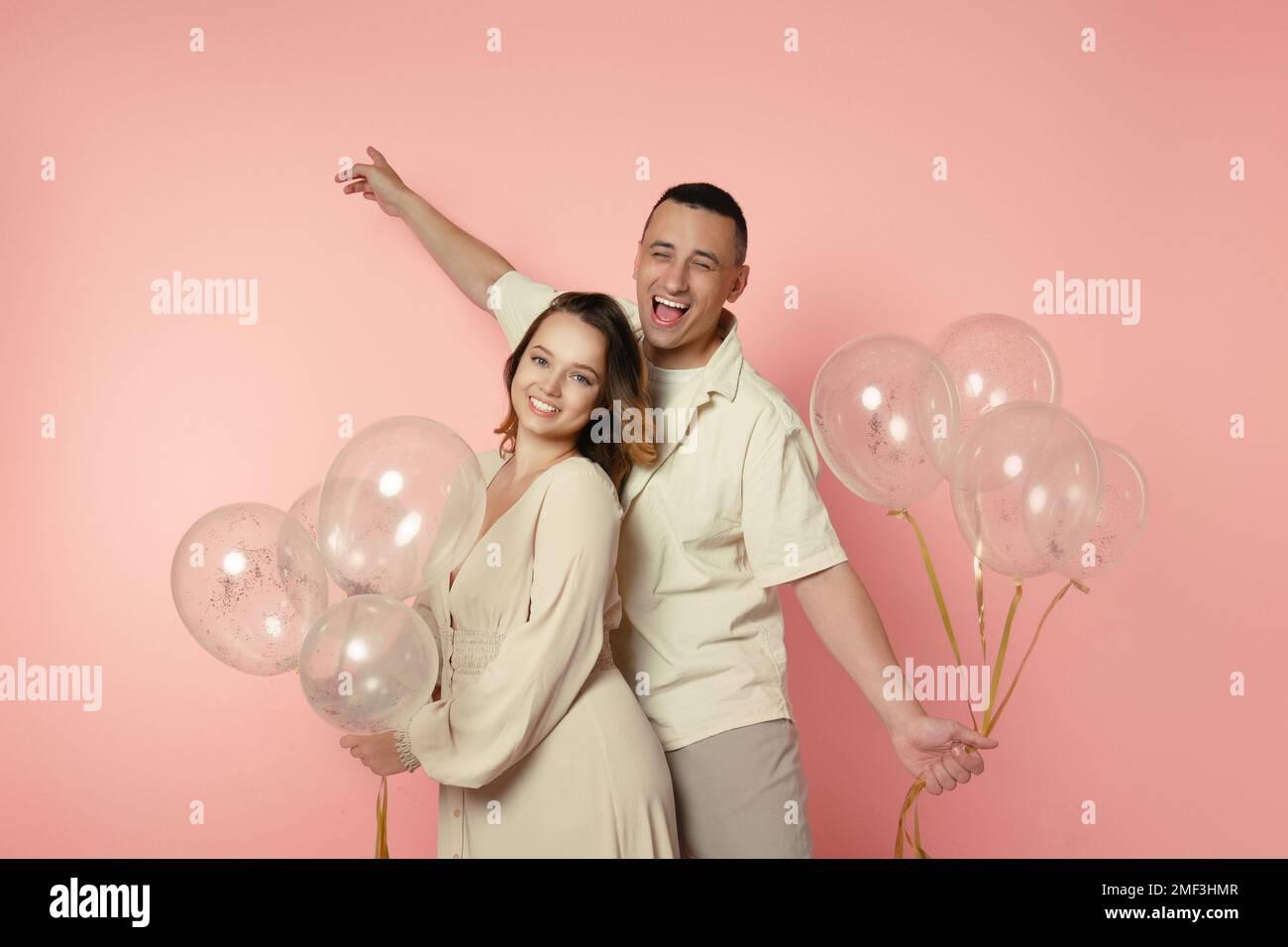Ein junges Paar in Pastellkleidung, Ballons auf pinkfarbenem Hintergrund. Liebhaber feiern und lächeln. Frau in langem Kleid, romantisches Foto mit Mann, Dating, Dan Stockfoto