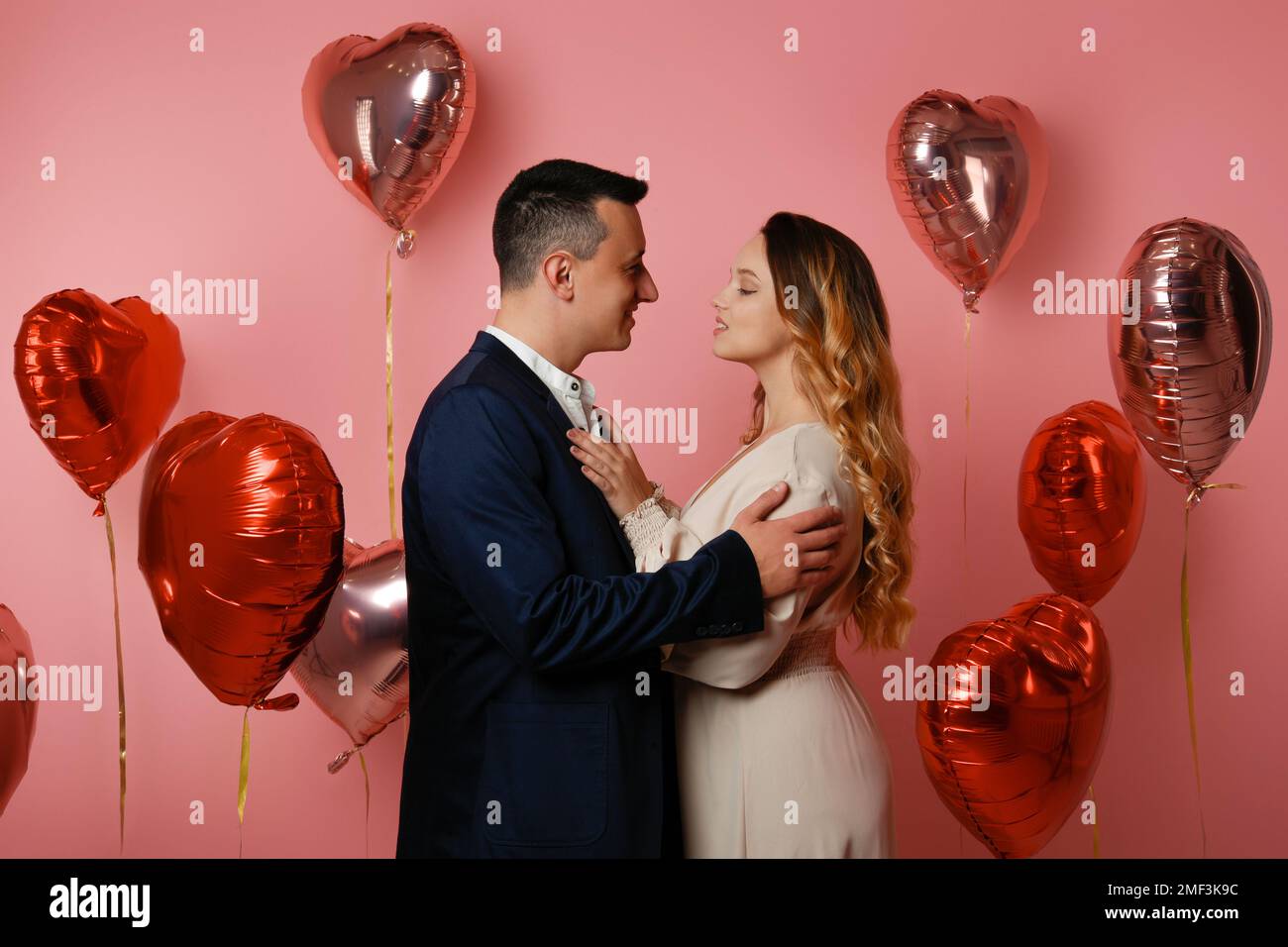 Eine Frau in einem Kleid und ein Mann im Anzug auf dem Hintergrund von Herzballons. Love on Valentine's Day, Romance and love, datiert am 14. Februar. Wunderschön Stockfoto