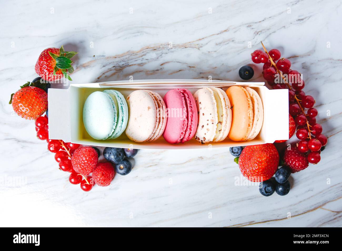 Macaron Dessert, eine Schachtel mit bunten Makronen, liegt auf einem Marmorstil. Süßigkeiten, Diät, Geschenk für den 8. März oder 14. Februar. Erdbeeren und Preiselbeeren, b Stockfoto