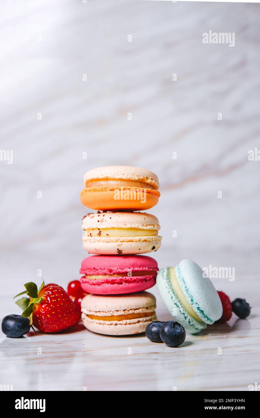 Macaron-Pink, Orange und Beige, Blau auf Marmor. Ein wunderschönes französisches Dessert. Früchte, Erdbeeren und Preiselbeeren, Heidelbeeren, r. Stockfoto
