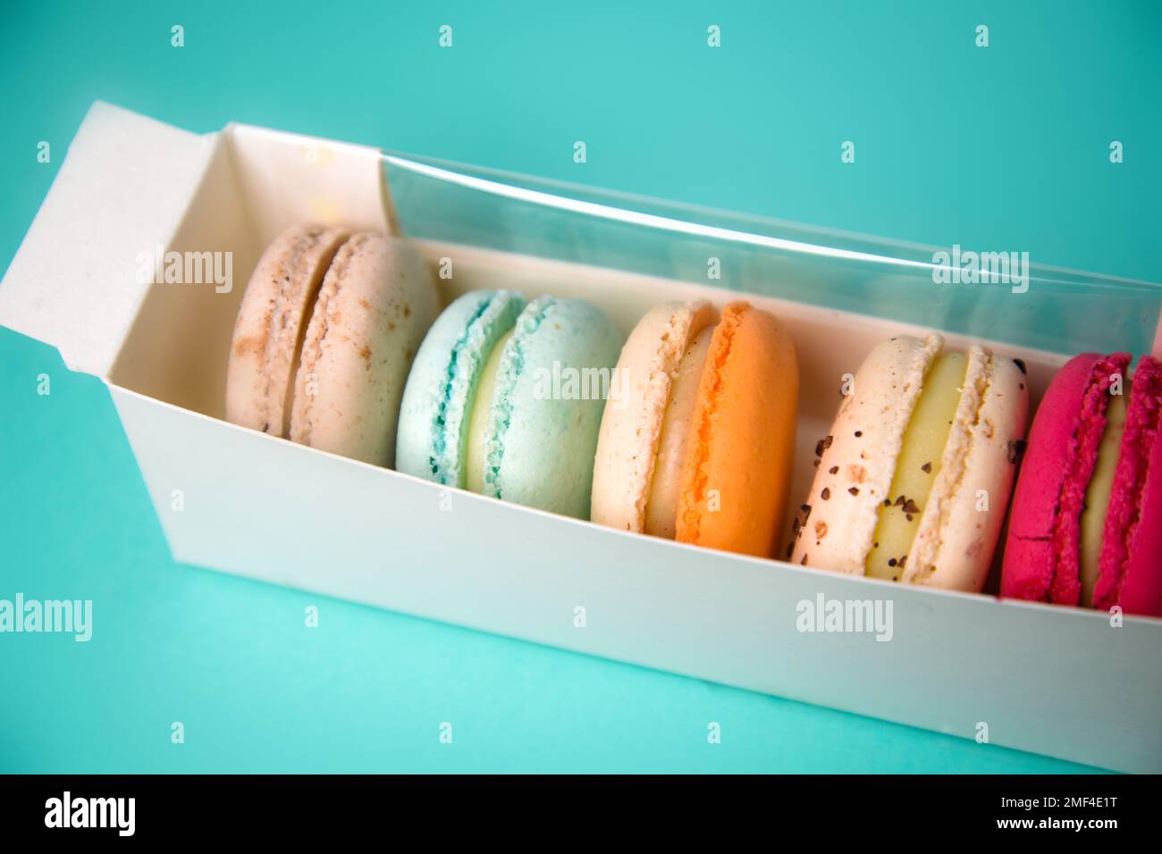 Bunte Makronen. Kleine französische Kuchen. Süße und farbenfrohe französische Makronen in einer Box auf blauem Hintergrund. Geschenk zum Valentinstag Stockfoto