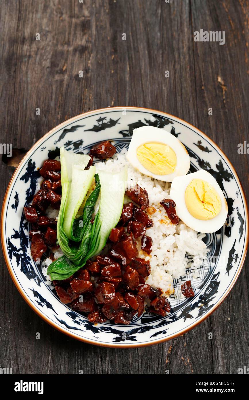 Taiwanesisches geschmortes Schweinefleisch Lu Rou Fan über weißem gedämpftem Reis mit gekochtem Ei und grünem Pakchoy. Auf Einem Holztisch Stockfoto