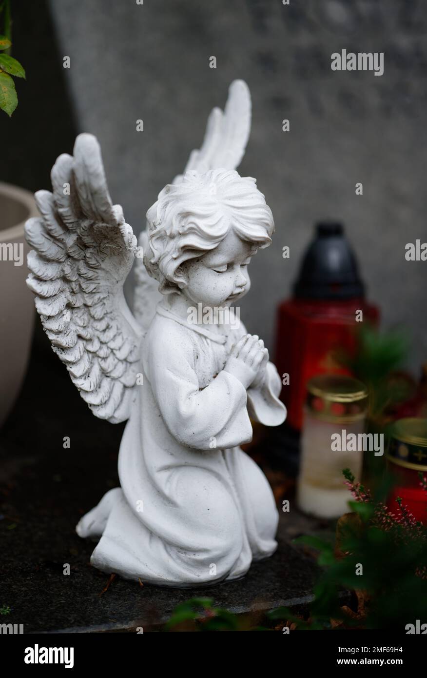 Kleine weiße betende Engelsfigur auf einem Grab mit Grabkerzen auf verschwommenem Hintergrund Stockfoto
