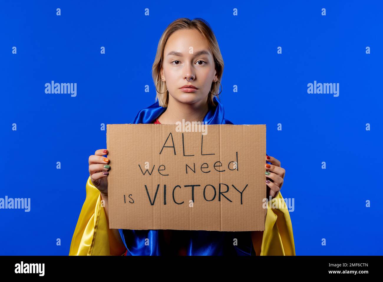 Ukrainerin mit Pappe alles, was wir brauchen, ist Sieg auf blauem Hintergrund. Stockfoto