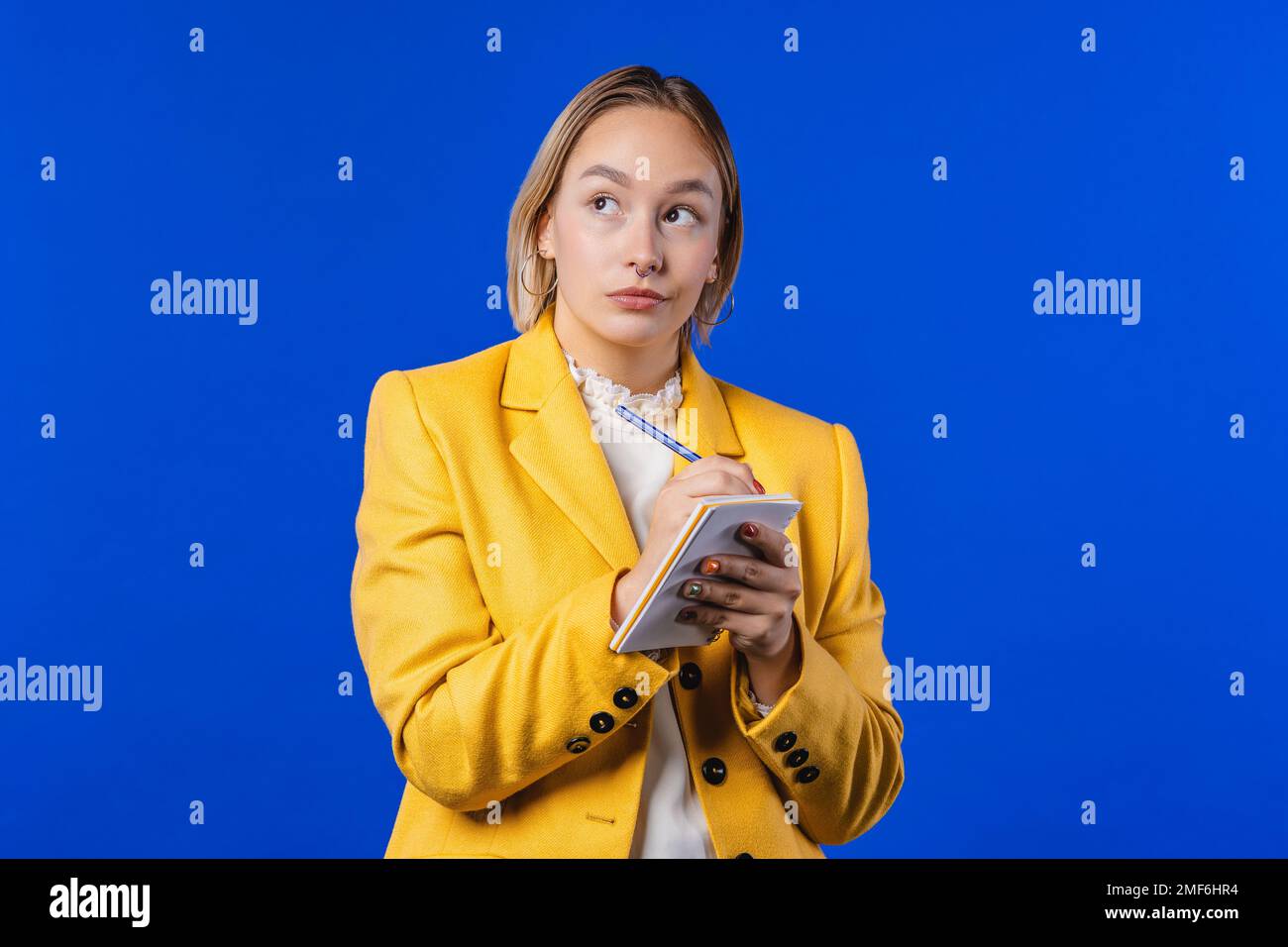 Eine bunte Frau, die Notizen im Planer schreibt. Blondes Mädchen, das über Zukunftspläne nachdenkt Stockfoto