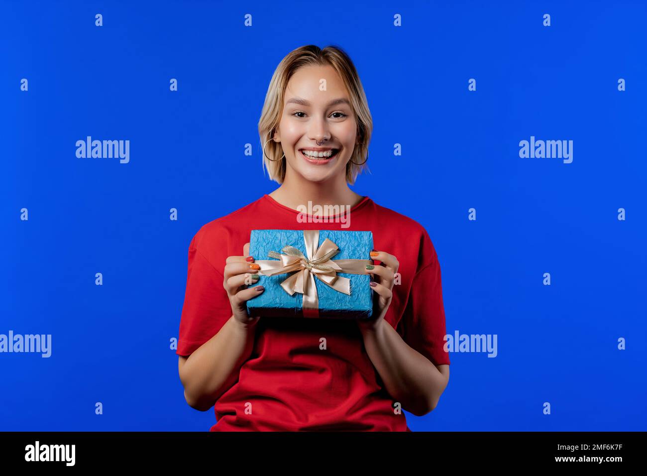 Geburtstagsfrau blondes Haar mit Geschenkbox auf blauem Hintergrund. Lächelndes Mädchen. Stockfoto