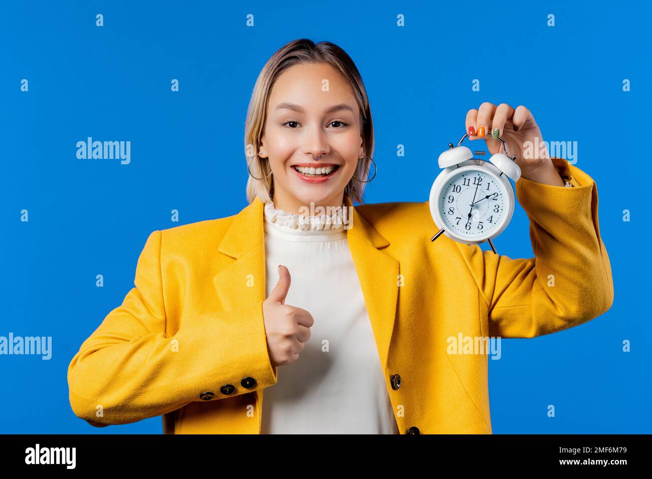 Glückliche Studentin in Gelb mit Wecker auf blauem Hintergrund. Früh am Morgen. Stockfoto
