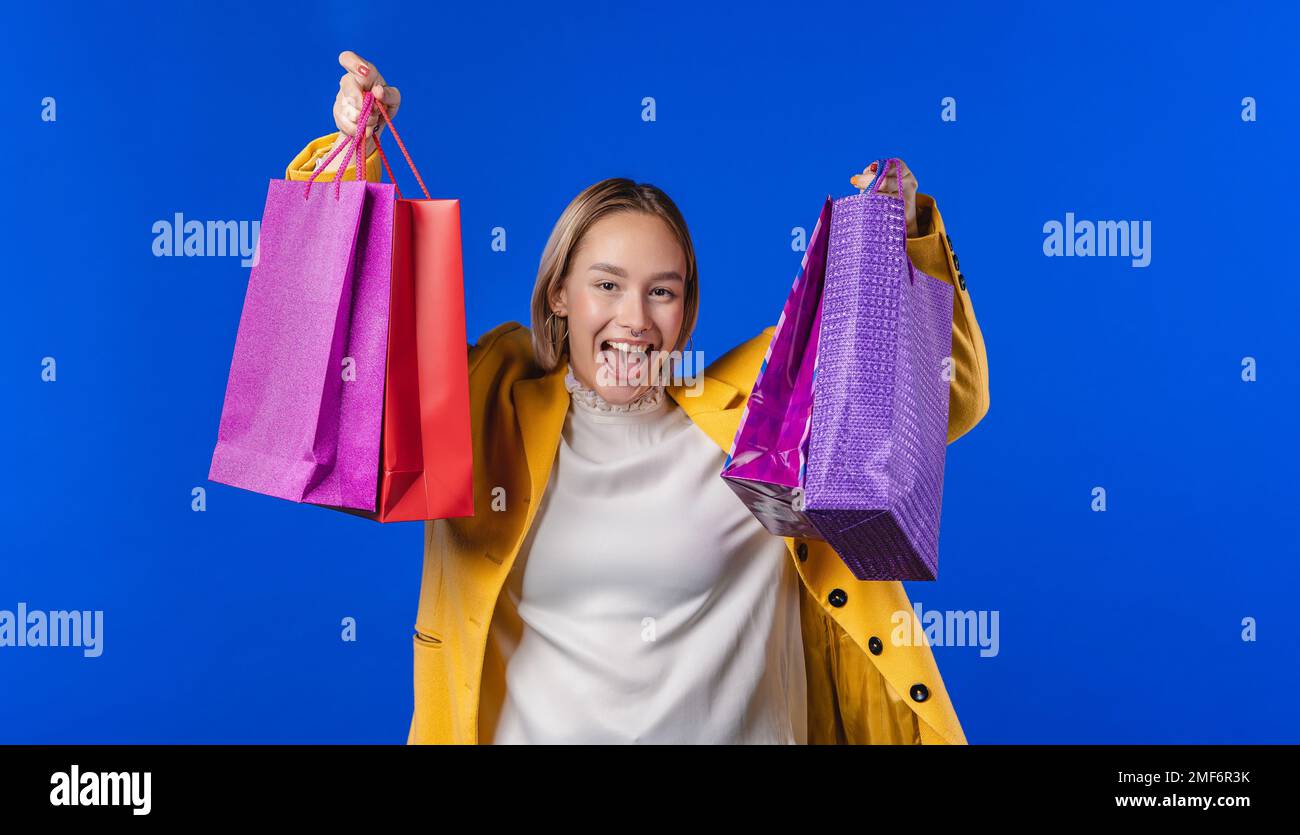 Aufgeregte Frau mit bunten Papiertaschen nach dem Einkauf auf blauem Studiohintergrund. Stockfoto