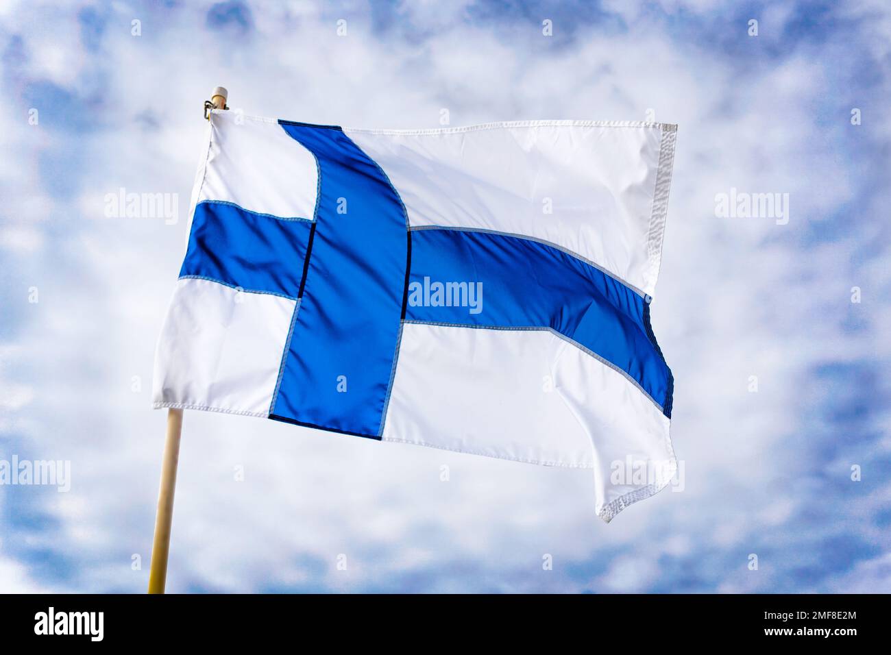 Staatsflagge der Republik Finnland, die im Wind mit blauem Hintergrund fließend ist. Stockfoto