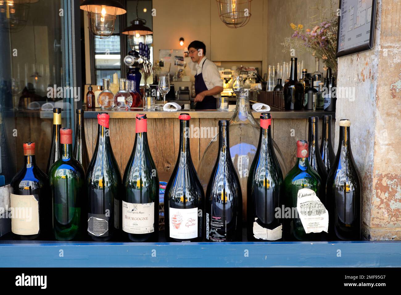 Leere Weinflaschen schmückten das Fenster eines französischen Restaurants mit einem männlichen Restaurantangestellten im Hintergrund. Paris. Frankreich Stockfoto