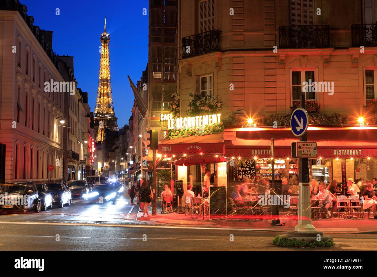 Nachtsicht auf den Eiffelturm und das Café Le Recrutement an der Ecke Rue Saint-Dominique und Boulevard de la Tour-Maubourg mit Rücklichtpfaden. Paris. Frankreich Stockfoto